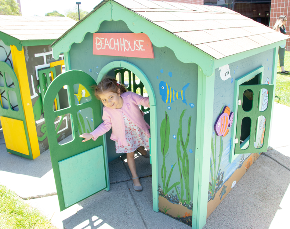 Little girl opening door to her beach-themed playhouse