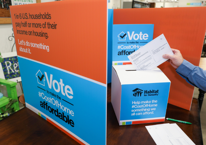 a person inserting a postcard into a box to vote