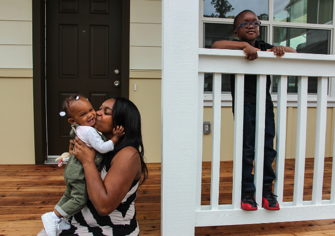 mother embracing her children in front of Habitat home.