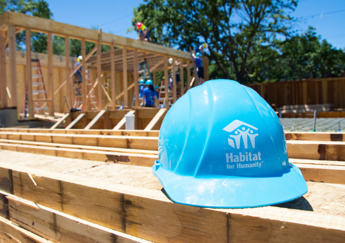 blue Habitat for Humanity hard hat sitting on a two by four piece of wood.